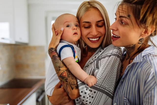 gay parents holding their baby at home smiling together