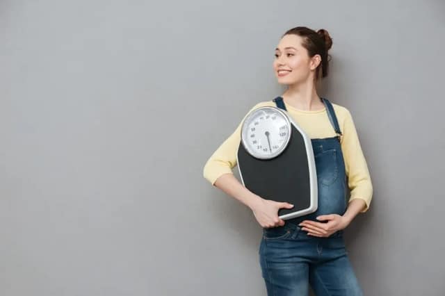 pregnancy weight gain concept with smiling pregnant woman holding a bathroom scale during maternity journey