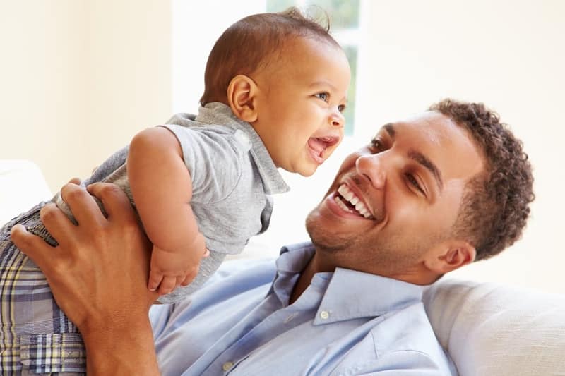 Smiling father playing with his baby son at home