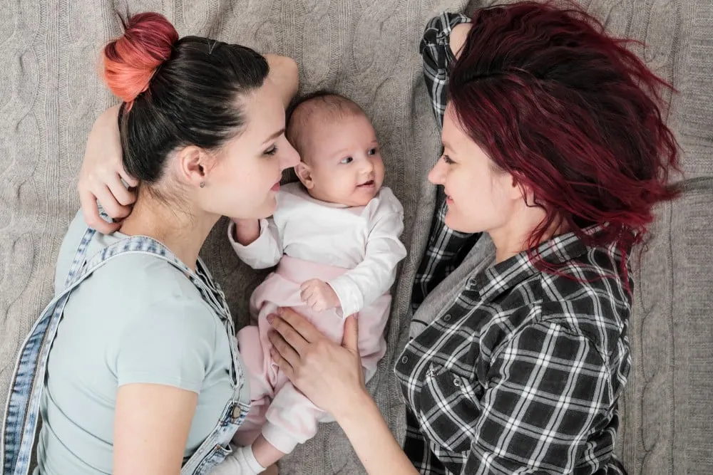 Two young women in casual clothes lying with their baby showing gay lesbian couples want a child through co-parenting or donor conception