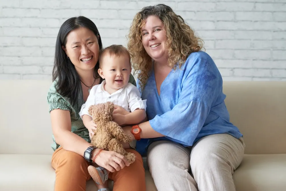 Lesbian IVF: same sex female couple with baby smiling together on sofa