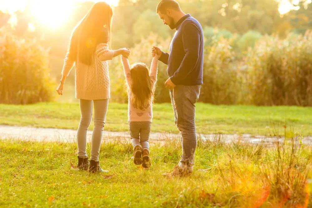 Shared parenting parents holding child hands walking together outdoors at sunset