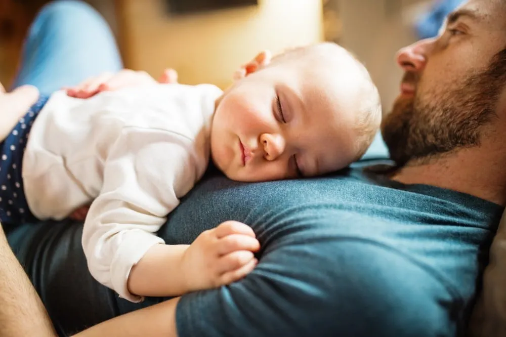 Dad bonding with baby while infant sleeps peacefully on father’s chest