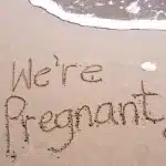 Pregnancy announcement written in sand on beach with message “We are pregnant”