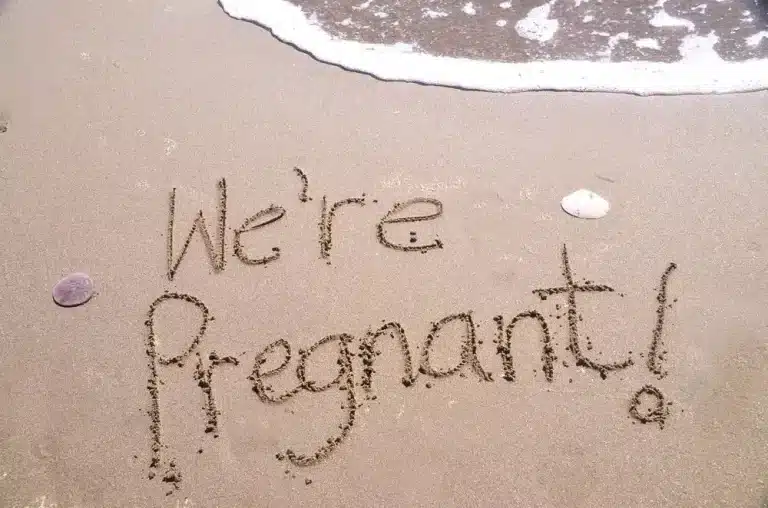 Pregnancy announcement written in sand on beach with message “We are pregnant”
