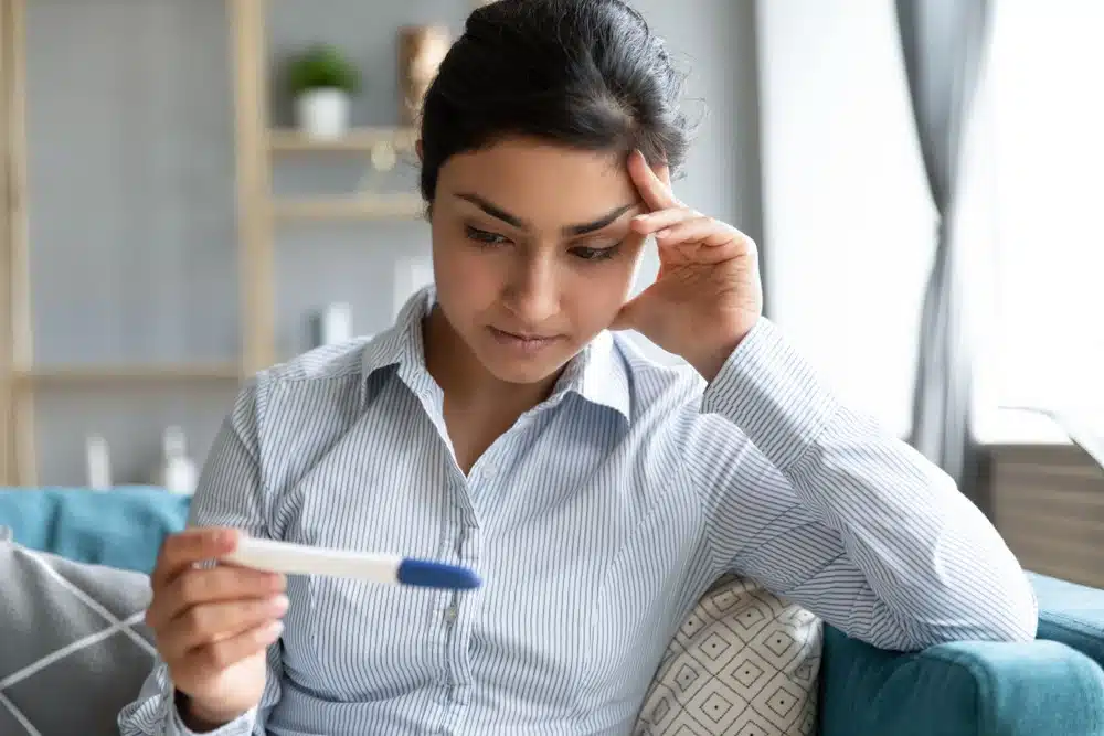 Worried infertile Indian girl holding pregnancy test